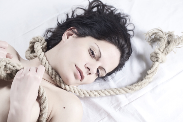 Woman lying in bed with bondage rope.