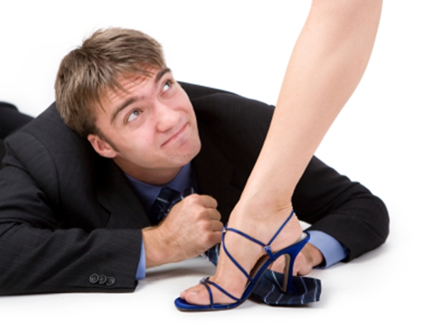 Man on floor enjoying foot fetish roleplay with woman who stands on his tie.
