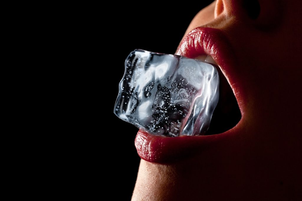 Woman holding an ice cube in her teeth for cold sensation play.