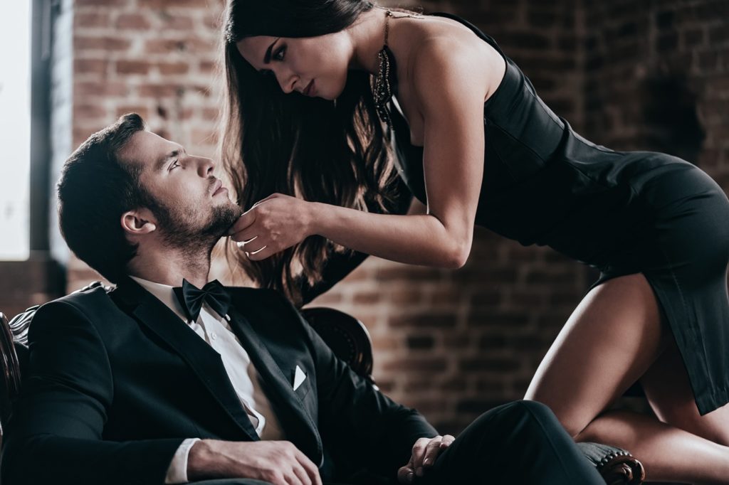 Woman leaning over man with hand on his face, preparing for BDSM face slapping.